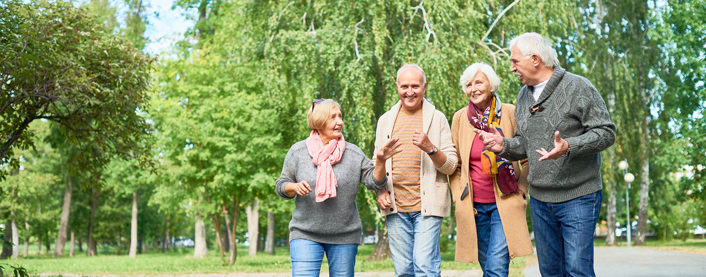 Four seniors friends have a conversation as they walk through a park